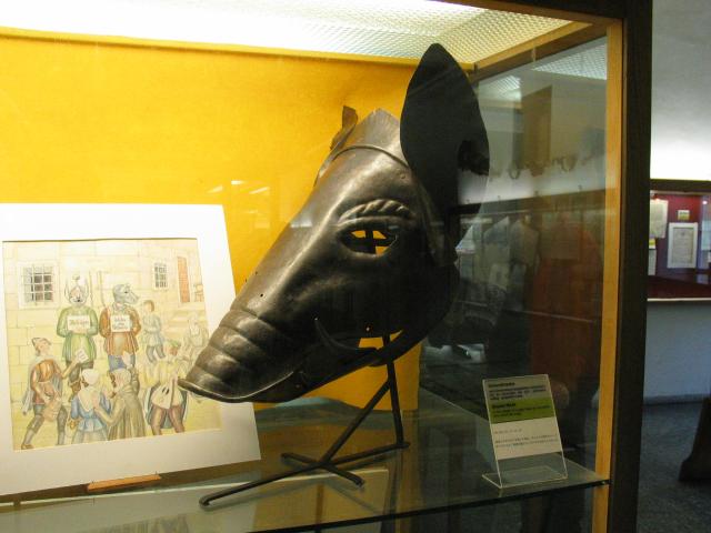 A shame mask in the Rothenburg Medieval Crime Museum.  People who had offended public decency had to wear these masks as penance, as shown in the illustration.  This one was used for people who displayed piggish behavior.