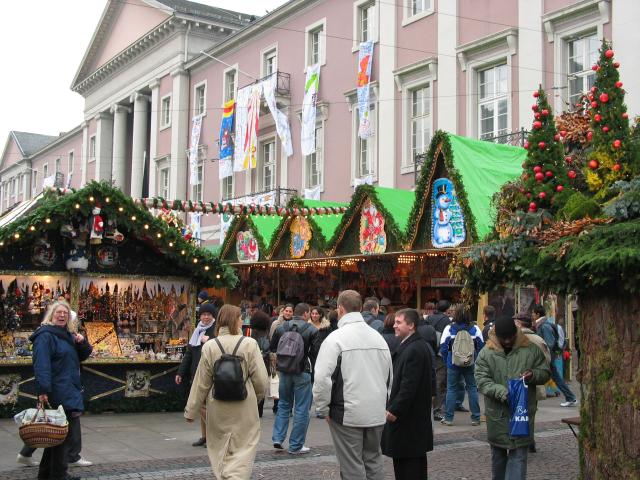 A view of the Karlsruhe Christmas market, showing the general flavor of the scene with the crowds, the many booths, and the banners flying on City Hall in the background.