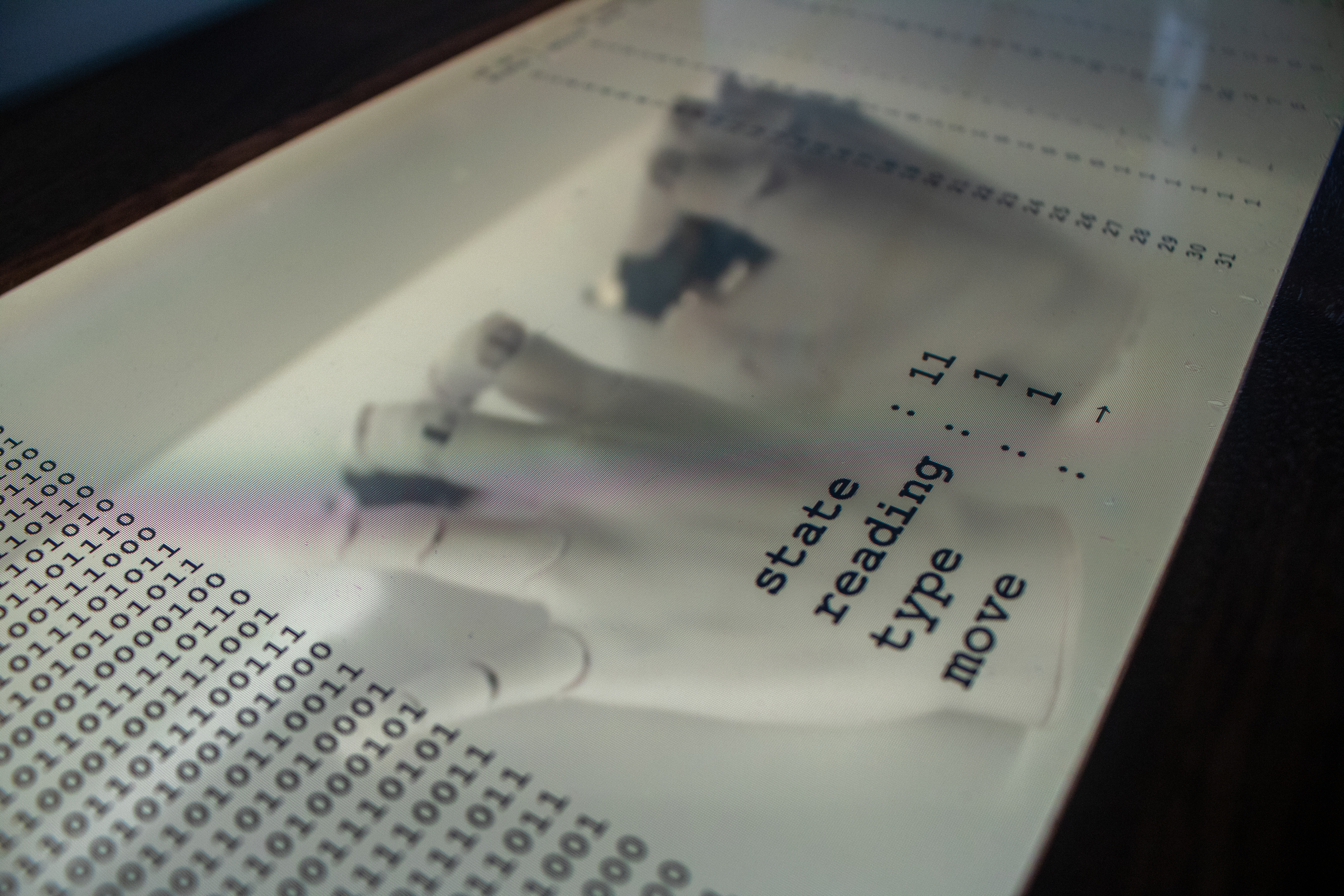 Transparent LCD Display. The text on the screen (e.g. memory snapshot, human-readalbe program being edited, current state machine information) changes in real time as the hands edit their code.