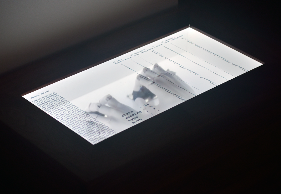 Autopoietic Turing Machine ceaselessly hacking away at itself independently in a darkened art gallery.