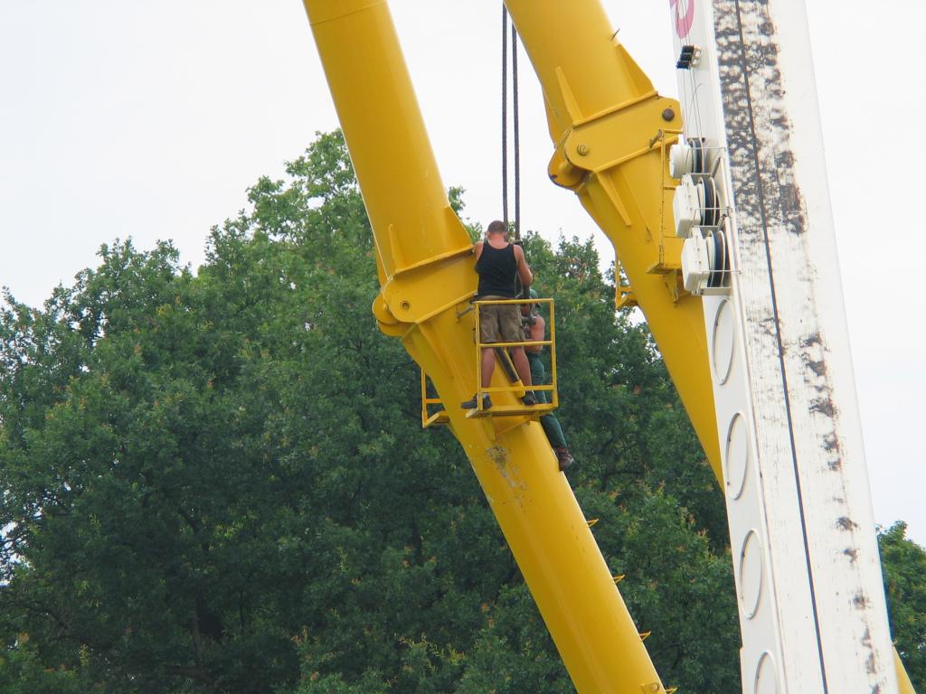 How to take apart a giant Ferris wheel, day two.  We were wondering
how they were going to get the main support beams down.  By the time
we arrived, the four outer ones had been removed and stacked on a
truck, but they were just getting ready to do the inner ones.  Here,
the crane has already been connected to a beam so that it won't drop
suddenly.  Two men then removed one of the connecting pins; the other
served as a hinge that was then lowered until it dangled freely.