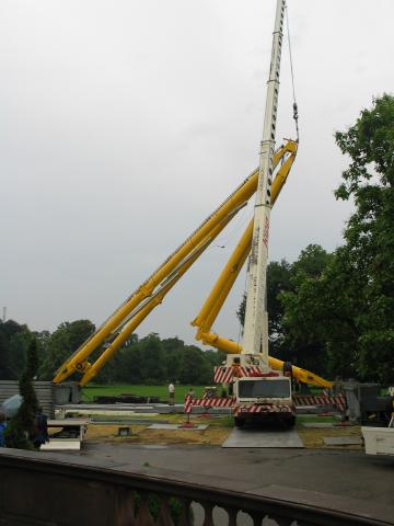 Lowering the main supports.  It's hard to see in this photo, but the
crane cable is carefully led up to the peak of the structure, where
there is a small U-shaped bracket that keeps it from slipping
sideways.  That turns out to be important, because by now, the support
point needs to be at the peak rather than halfway down a beam.