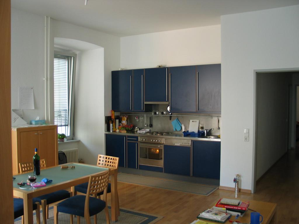 Our apartment.  This picture was taken from a corner of the living
room.  The windows are all double-paned for the winter, and also
double-hinged so that they can either lean out (as shown) or swing
open like a door.  The kitchen is tiny, but adequate.  The
refrigerator is the lower left "cupboard" and is about the size of a
hotel or office mini-fridge in the U.S.  The cabinet on the left was
intended for a stereo, but is now our pantry.  The coffee table was
intended as a TV table; the "coffee table" provided was so tiny that
we use it as an end table.  Note the wine bottle on the table, a
necessary fixture in any Kuenning household.