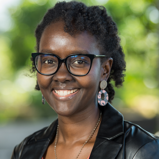An image of a black woman smiling with black glasses and a black jacket